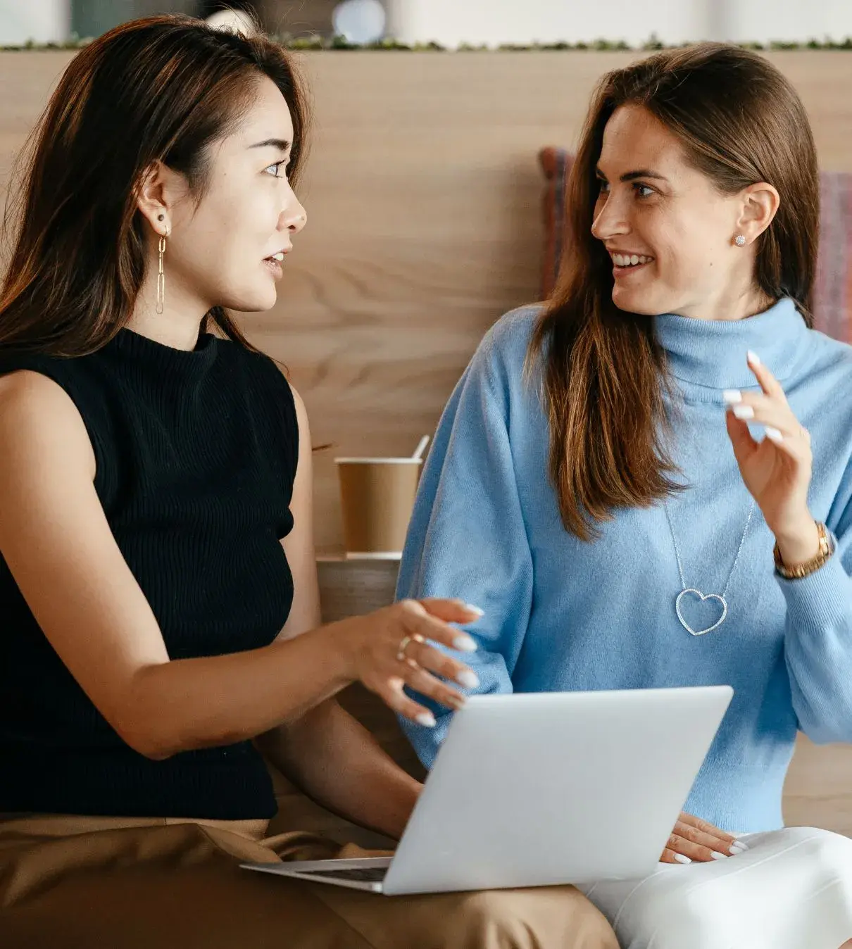 Two women collaborating over a laptop, one explaining and the other engaged and excited, showing a real-time strategic conversation